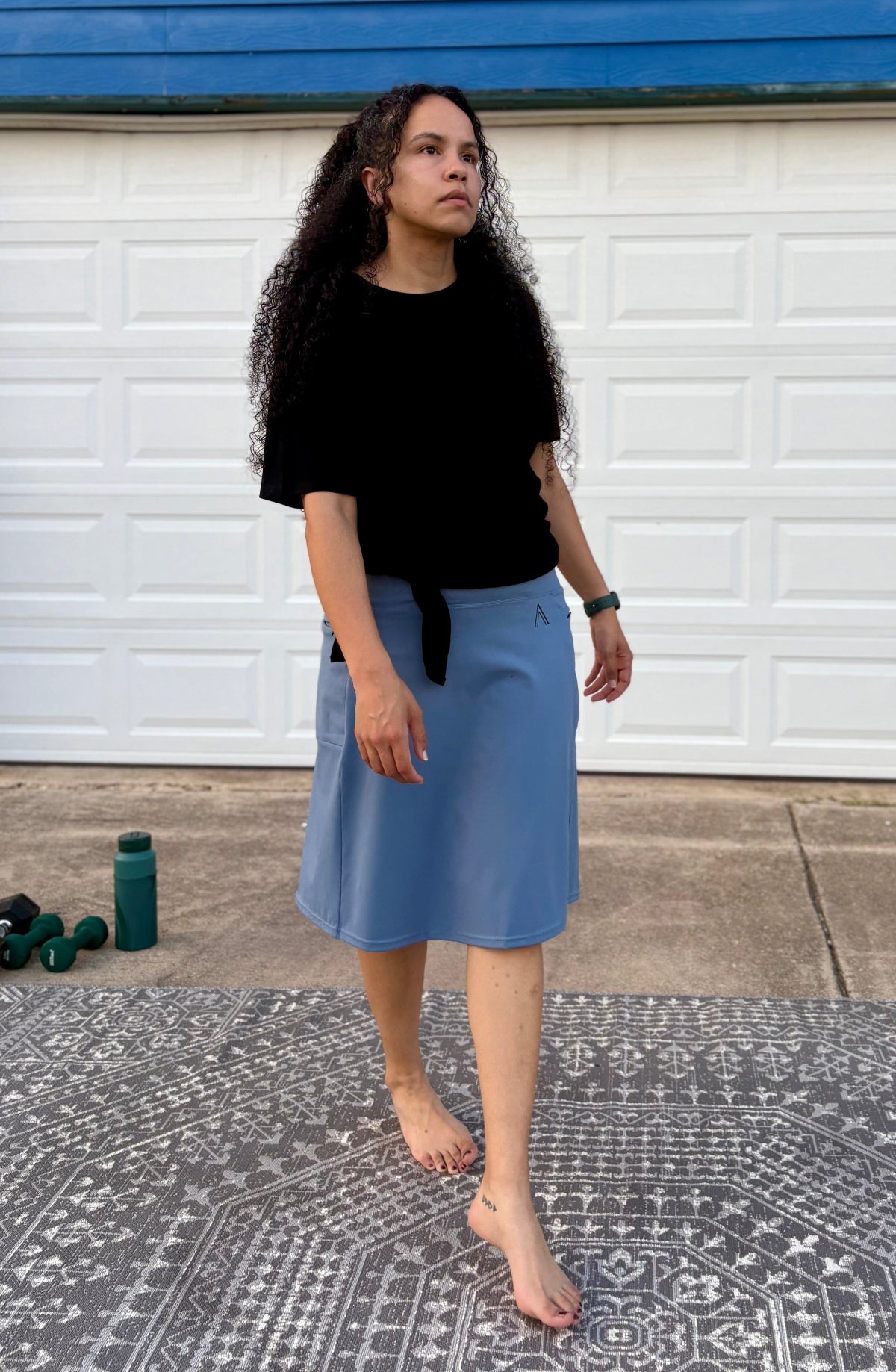 Woman wearing a black top and blue skirt standing in front of a white garage door.