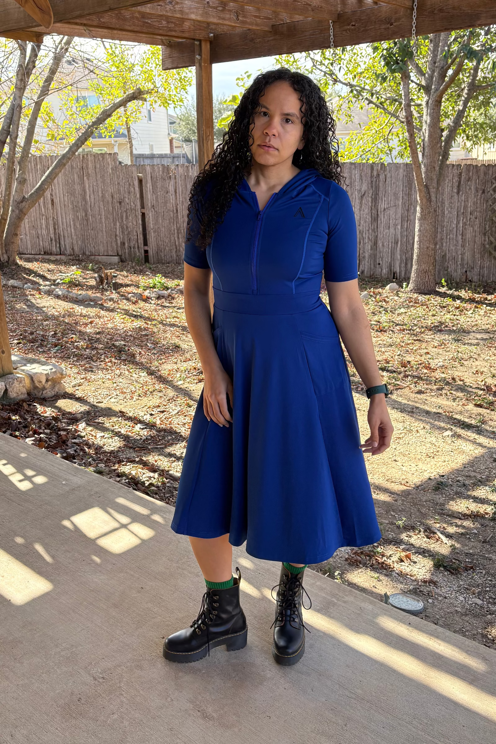 Woman in a blue dress standing under a wooden pergola with trees in the background
