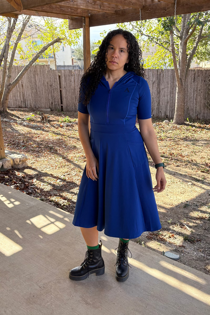 Woman in a blue dress standing under a wooden pergola with trees in the background
