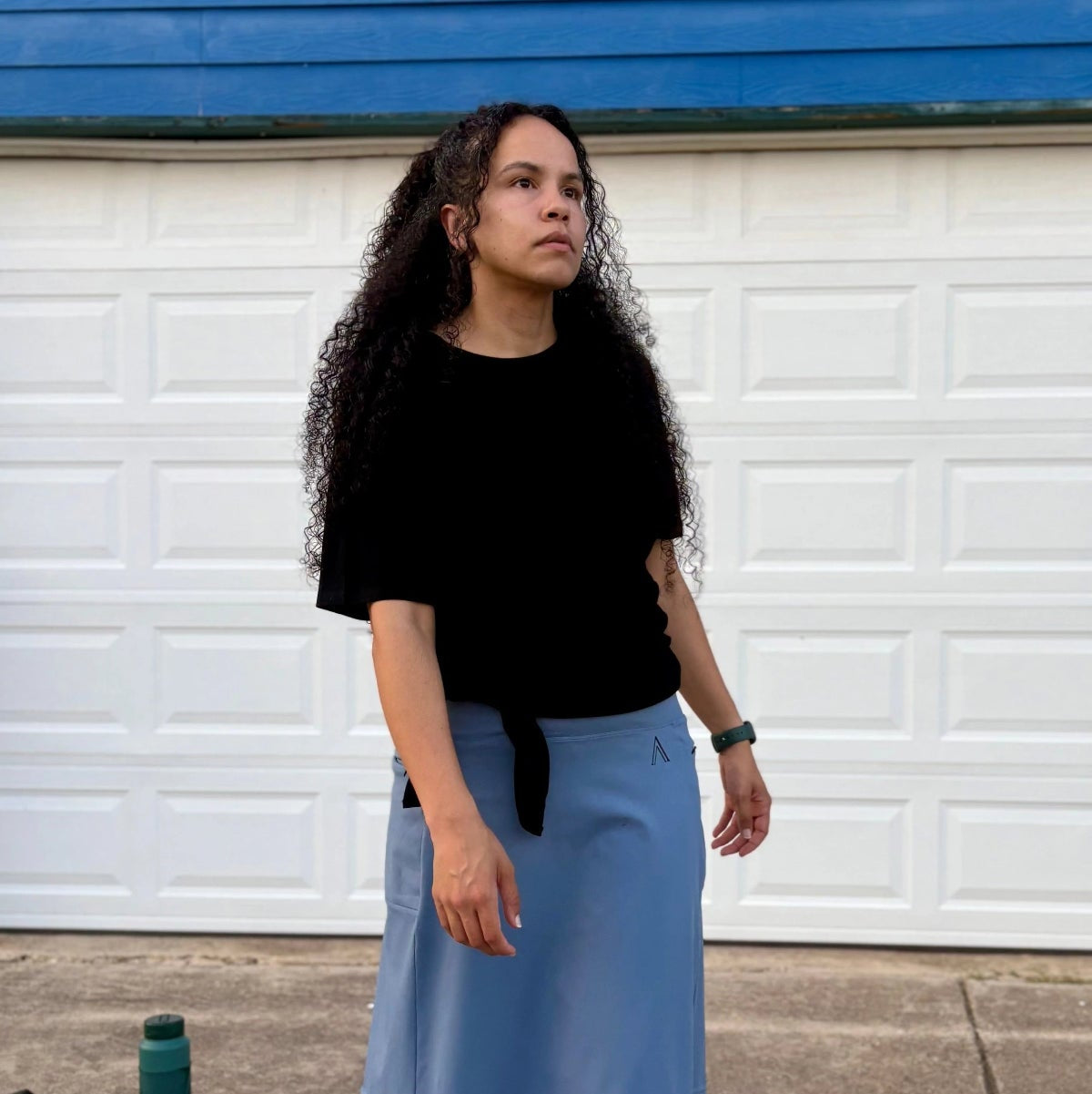 Woman wearing a black top and blue skirt standing in front of a white garage door.