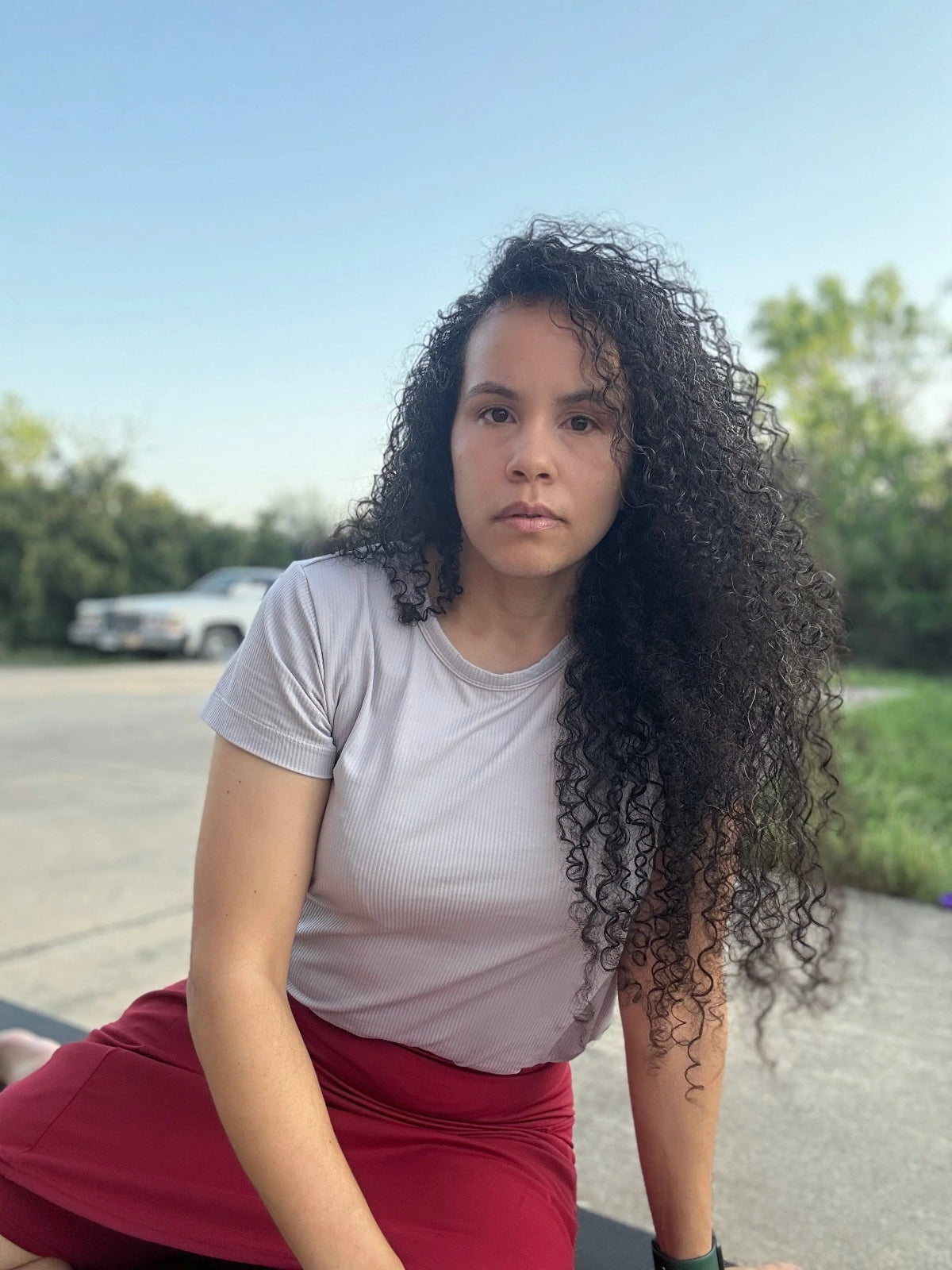 Person with curly hair wearing a white shirt and red skirt outdoors