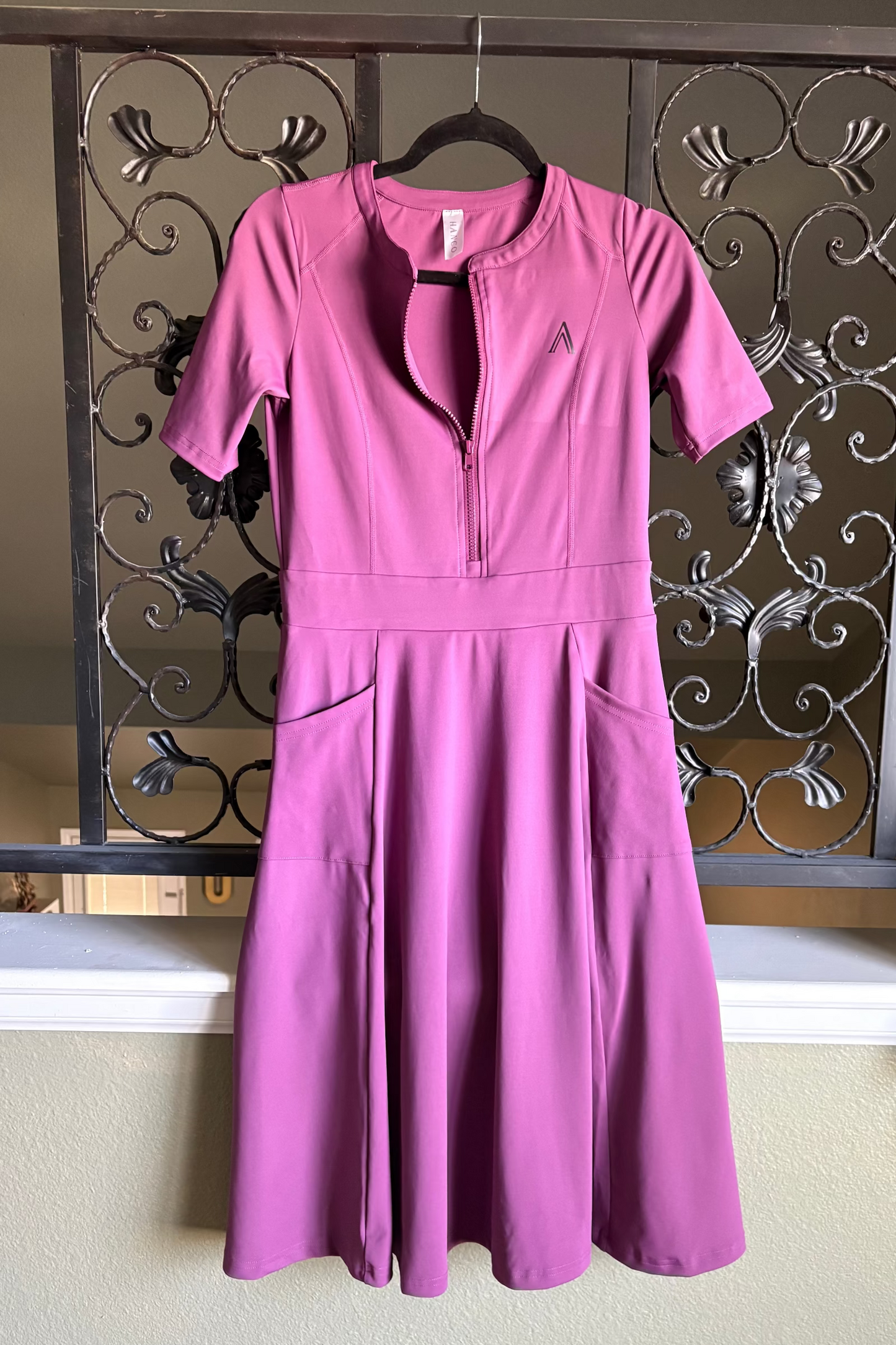 Pink dress hanging on a decorative metal rod against a neutral wall.