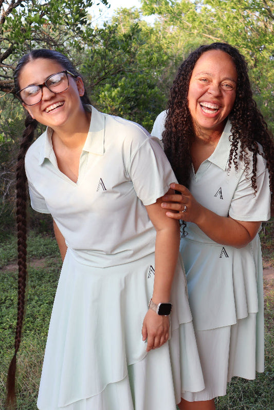 Three women in matching outfits standing outdoors with trees in the background