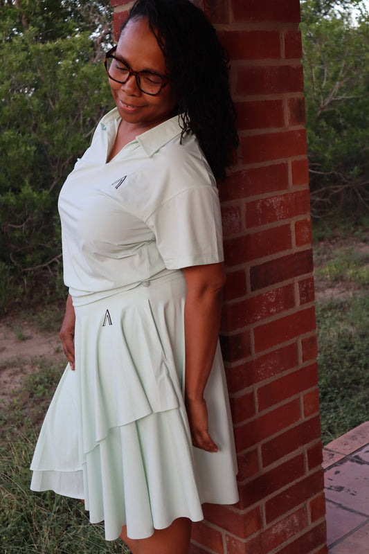 Person wearing a white dress with a brand logo, standing outdoors against a brick wall.